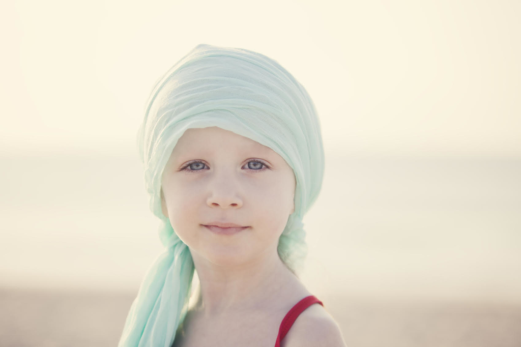 Image of young female chemotherapy patient wearing head scarf looking serenely at the camera
